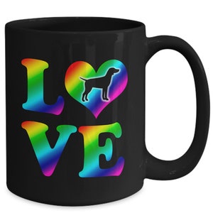 May include: Black ceramic mug with the word "LOVE" in rainbow gradient letters. A rainbow heart with a black dog silhouette is in the center. The mug has a curved handle and a glossy finish.