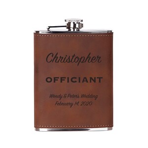 May include: Brown leather-wrapped flask with a silver top and engraved text: "Christopher Officiant Wendy & Peter's Wedding February 14, 2020".