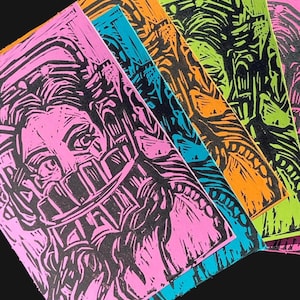 May include: A collection of colorful linocut prints. The prints feature black and white designs on pink, blue, orange, and green backgrounds. The designs appear to be abstract or stylized portraits and architectural elements.