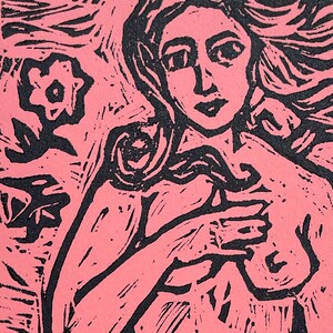 May include: A pink and black linocut print of a woman with long flowing hair. The woman is holding her arms across her chest. A flower and foliage are in the background. The art is a stylized, expressive representation.