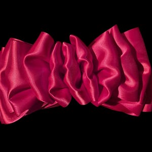 May include: A large, bright pink satin bow with a soft, flowing texture. The bow is tied in a loose knot and the ends are draped over each other.