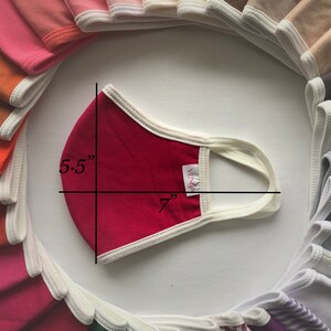 May include: A red face mask with white trim and elastic ear loops. The mask measures 7 inches wide and 5.5 inches tall.