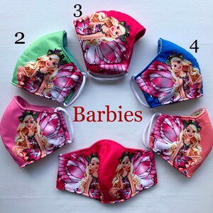 May include: Five pink, blue, and green fabric face masks with a white elastic band. Each mask features a different Barbie fairy design with pink wings and glitter. The masks are numbered 1 through 5.