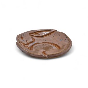 May include: A handmade ceramic dish in the shape of a rabbit. The dish is a mottled brown color with blue speckles and a raised rabbit design. The dish is ideal for holding small items.