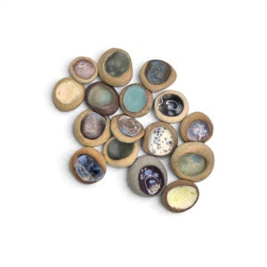 May include: A collection of fifteen small, rounded ceramic stones with a textured, tan-colored exterior and smooth, concave centers featuring various glossy glazes in shades of blue, purple, white, green, and brown, arranged in a cluster.