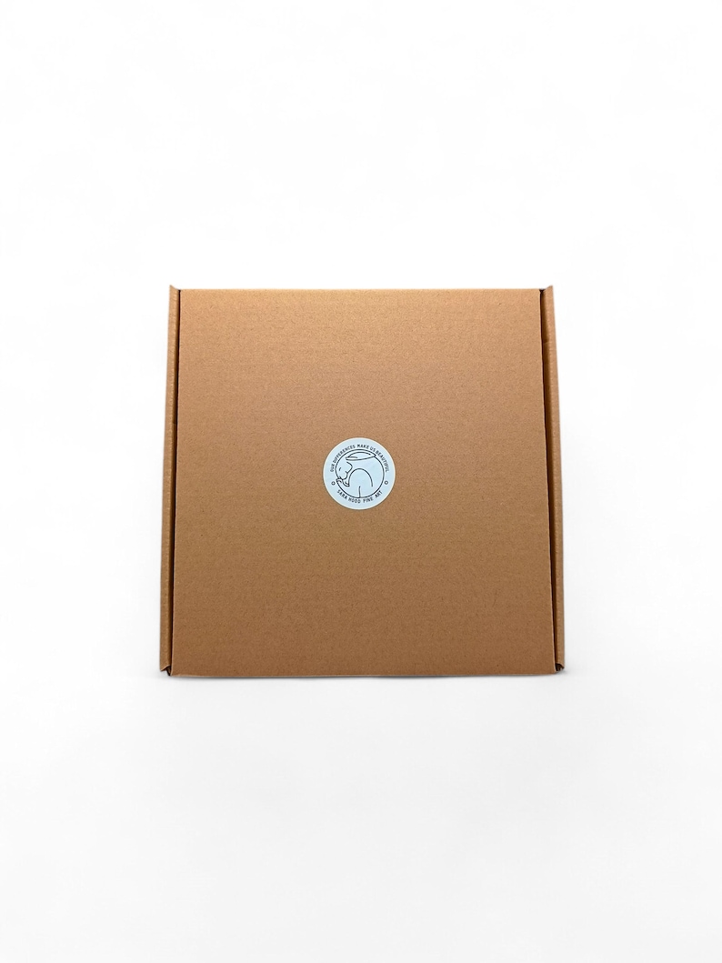 May include: A square, brown cardboard box with a circular sticker on the front. The sticker features a blue and white design with text. The box is centered on a white background.