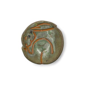 May include: A ceramic dish with a green glaze and a rabbit design in orange. The rabbit is depicted in a stylized, minimalist form. The dish has a rounded shape and is set against a white background.