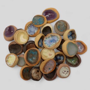 May include: A selection of small, ceramic pieces in organic shapes. They have a light brown exterior and feature interior colours like blue, purple, and cream. Some have a glossy finish. The pieces are of various sizes and textures.