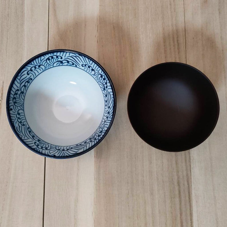 May include: Two bowls, one white with a blue and white wave pattern and one black.