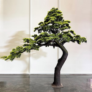 May include: A large, artificial bonsai tree with a dark brown, curved trunk and vibrant green foliage. The tree's branches extend gracefully, creating a natural, artistic form. The tree is set against a plain white background.