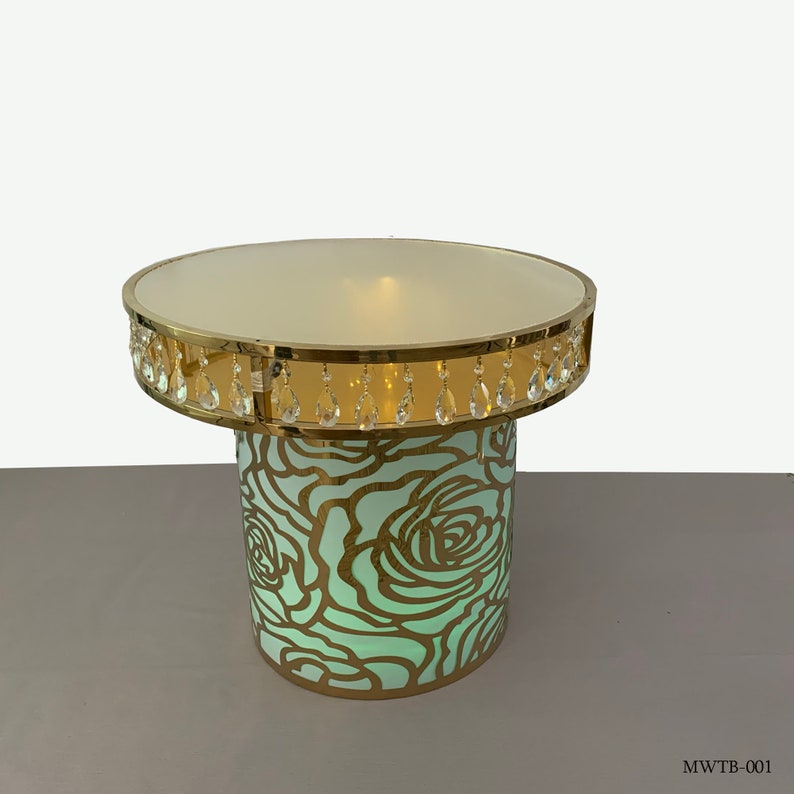May include: A gold metal table with a round, white top and a base with a cut-out design of green roses. The table has a crystal beaded trim around the top.