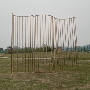 May include: Three gold metal archways with a curved top and vertical bars. The archways are standing on a grassy field.