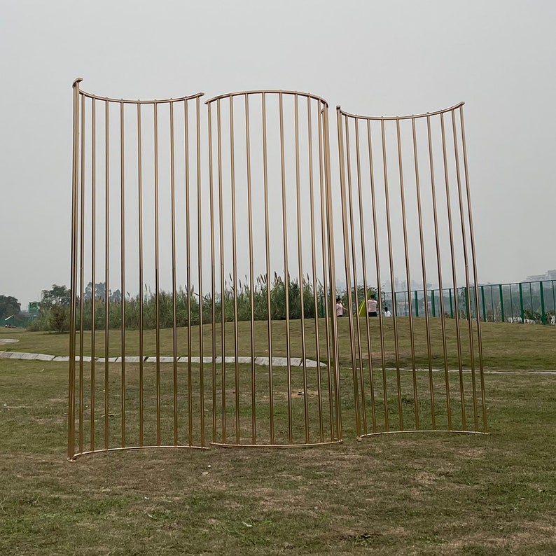 May include: Three gold metal archways with a curved top and vertical bars. The archways are standing on a grassy field.