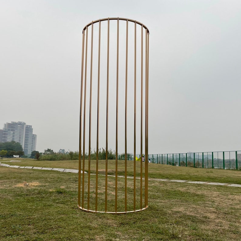 May include: A gold metal archway with a circular top and vertical bars. The archway is standing on a grassy field.