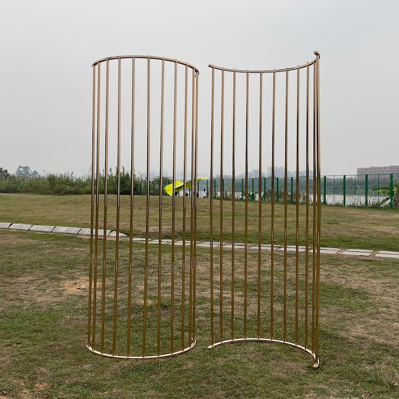 May include: A gold metal backdrop with a curved design. The backdrop is made of thin metal bars and is freestanding.