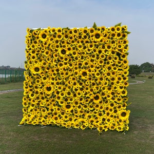 Puede incluir: Una pared cubierta de girasoles artificiales amarillos. Los girasoles están dispuestos en un patrón denso, creando un fondo vibrante y alegre.