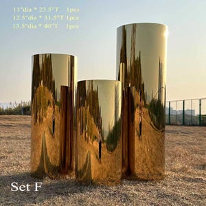 Puede incluir: Conjunto de tres pedestales cil&iacute;ndricos dorados. El m&aacute;s grande mide 101.6 cm de alto y 34.3 cm de di&aacute;metro. El pedestal mediano mide 80 cm de alto y 31.8 cm de di&aacute;metro. El m&aacute;s peque&ntilde;o mide 59.7 cm de alto y 27.9 cm de di&aacute;metro. El texto "Set F" est&aacute; en la parte inferior.