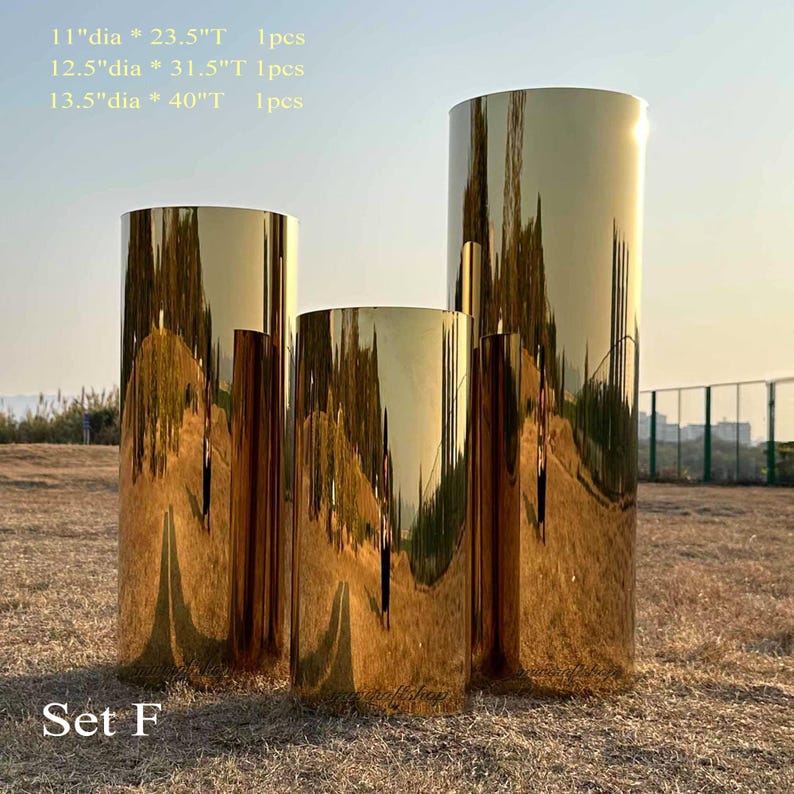 Puede incluir: Conjunto de tres pedestales cil&iacute;ndricos dorados. El m&aacute;s grande mide 101.6 cm de alto y 34.3 cm de di&aacute;metro. El pedestal mediano mide 80 cm de alto y 31.8 cm de di&aacute;metro. El m&aacute;s peque&ntilde;o mide 59.7 cm de alto y 27.9 cm de di&aacute;metro. El texto "Set F" est&aacute; en la parte inferior.