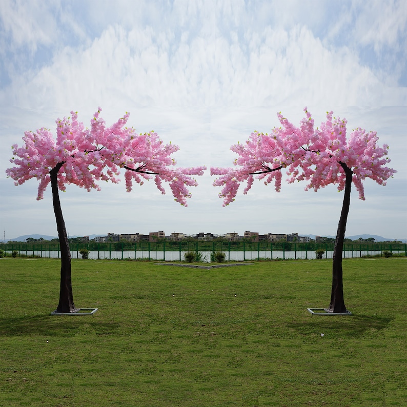 May include: Two pink artificial cherry blossom trees with green grass in the background.
