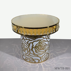 May include: A gold and white round table with a crystal beaded trim. The table top is smooth and the base features a white cutout design of roses.
