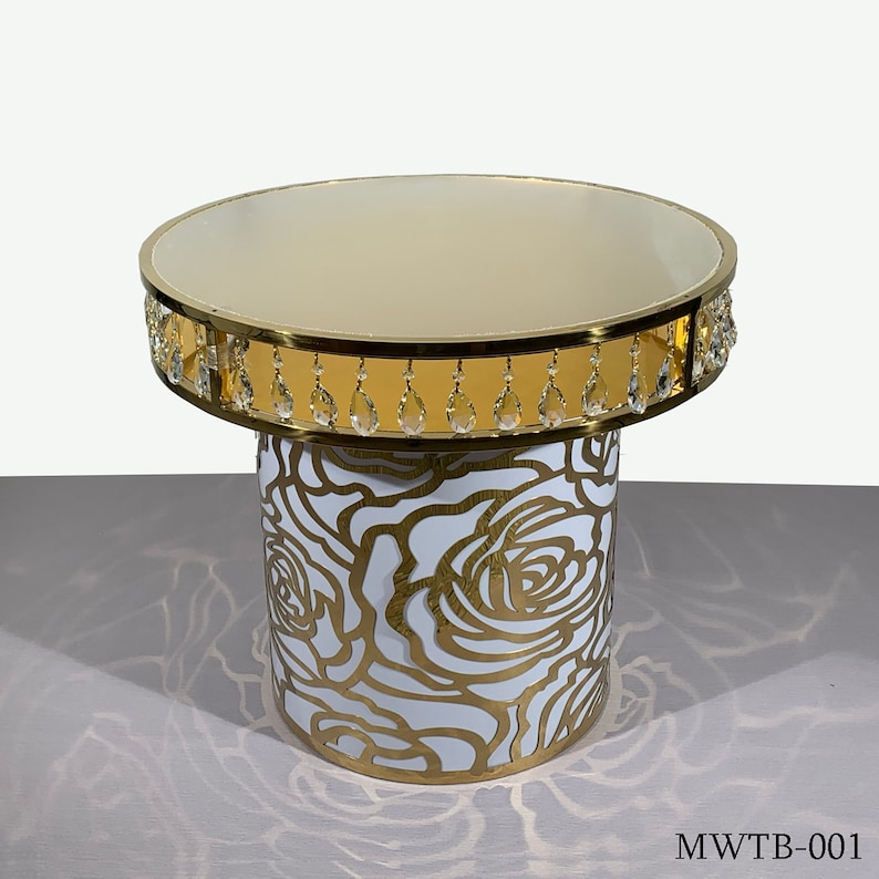 May include: A gold and white round table with a crystal beaded trim. The table top is smooth and the base features a white cutout design of roses.