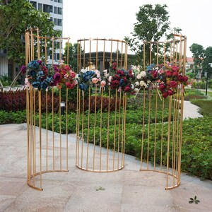 May include: Three gold metal archways with a curved top and vertical bars. The archways are decorated with artificial flowers in shades of red, pink, blue, and white.