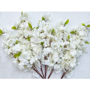 May include: A bunch of artificial white flower stems with green leaves. The flowers are clustered together and have a delicate, feathery appearance.