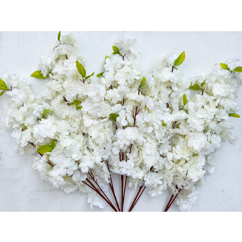 May include: A bunch of artificial white flower stems with green leaves. The flowers are clustered together and have a delicate, feathery appearance.