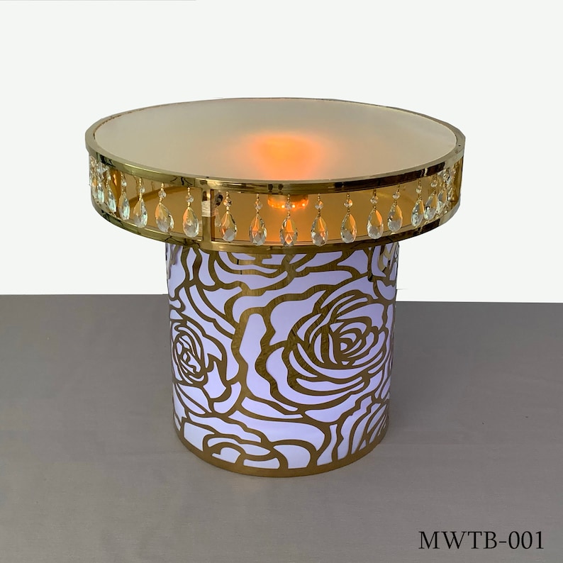 May include: A gold metal table with a round top and a white rose pattern. The table has a clear glass top and a row of crystal drops around the edge.