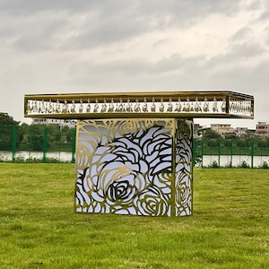 May include: A gold metal table with a rose pattern design and crystal accents. The table is on a green grassy lawn.