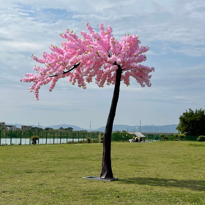 May include: A pink artificial cherry blossom tree with a brown trunk, standing on a green grassy lawn.