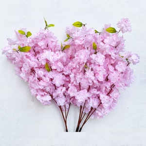May include: A bouquet of artificial pink cherry blossom branches with green leaves.