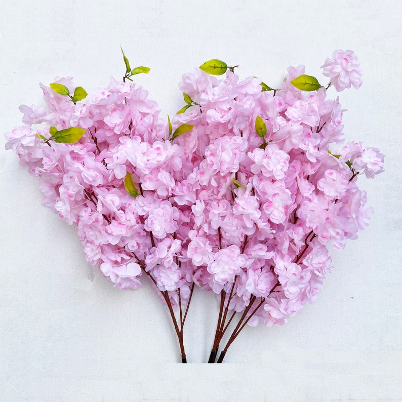 May include: A bouquet of artificial pink cherry blossom branches with green leaves.