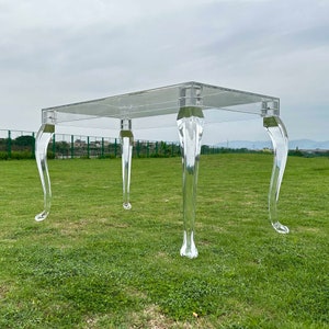 以下が含まれることがあります： 4本の脚が付いた透明なアクリル製のテーブル。テーブルは長方形の天板で、脚は曲がっており、クラシックなデザインです。