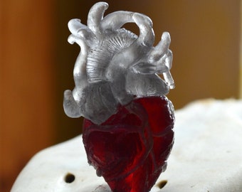 May include: A red glass heart with a silver anatomical heart sculpture on top.