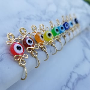 May include: A set of rainbow colored evil eye charms with gold wire wrappings. The charms are in a rainbow order, starting with red and ending with purple.