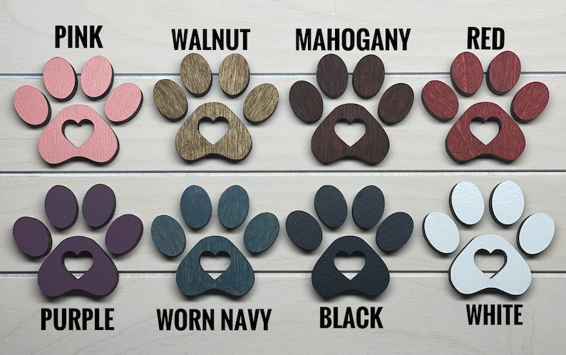 May include: Eight wooden paw prints with a heart cutout in the center, painted in various colors: pink, walnut, mahogany, red, purple, worn navy, black, and white.