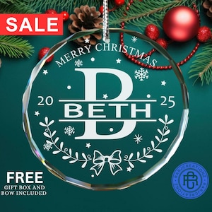 May include: A clear, faceted Christmas ornament with the name "BETH" in white script. The ornament has a bow, snowflakes, and the text "MERRY CHRISTMAS" and "2025". A red "SALE" banner is in the top left corner.