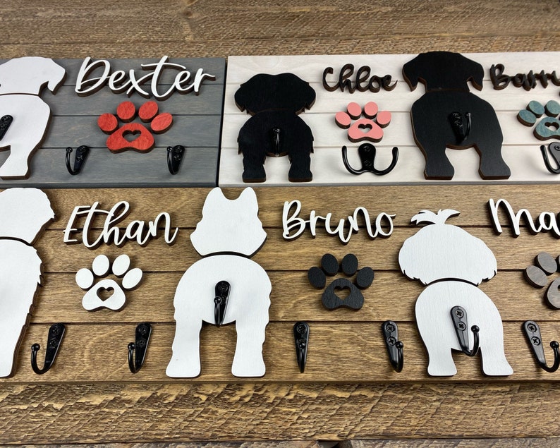 May include: Wooden dog leash rack with four hooks. The rack features four dog silhouettes with paw prints and names: Dexter, Chloe, Bruno, and Max. The rack is painted in shades of gray, white, and brown.