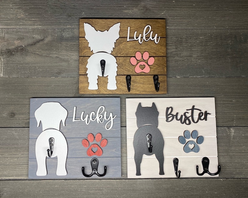 May include: Three wooden dog leash hooks with paw prints and dog silhouettes. The hooks are labeled "Lulu", "Lucky", and "Buster".