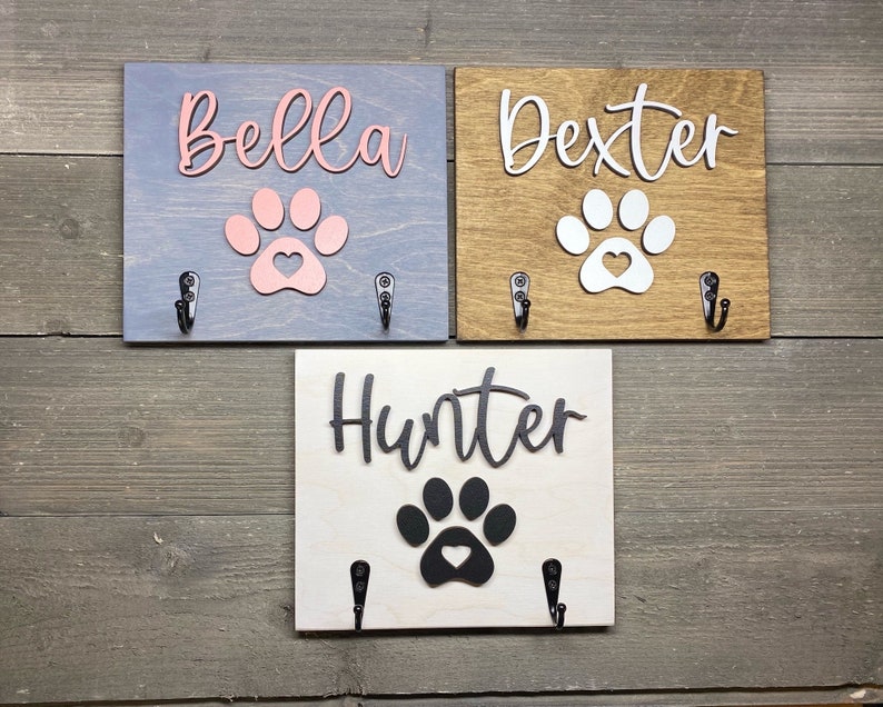 K&ouml;nnte beinhalten: Drei Haken aus Holz f&uuml;r Hundeleinen mit Pfotenabdr&uuml;cken und personalisierten Namen: Bella, Dexter und Hunter. Jeder Haken hat zwei Metallhaken zum Aufh&auml;ngen von Leinen.