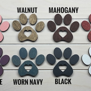 May include: Eight wooden paw prints with a heart cutout in the center, painted in various colors: pink, walnut, mahogany, red, purple, worn navy, black, and white.