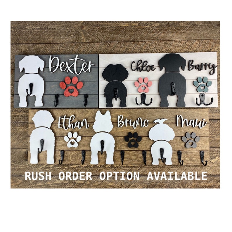 May include: A wooden dog butt key holder with five hooks. The key holder has a gray, white, and natural wood finish. The dog butts are painted white and black. The names Dexter, Chloe, Barry, Ethan, Bruno, and Maui are written on the key holder.