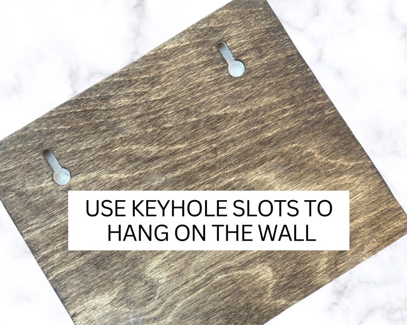May include: A dark brown wooden sign with two keyhole slots for hanging on a wall. The sign reads "USE KEYHOLE SLOTS TO HANG ON THE WALL".