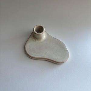 以下が含まれることがあります： 不規則で有機的な形をした白いセラミック製のキャンドルホルダー。ホルダーには、キャンドル用の丸い穴が1つあります。