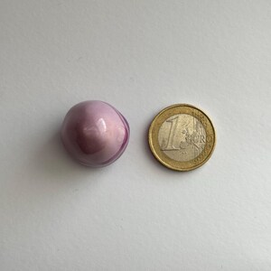 K&ouml;nnte beinhalten: Eine kleine, runde, violette und wei&szlig;e, irisierende Glasperle. Die Perle ist etwa so gro&szlig; wie eine 1-Euro-M&uuml;nze.