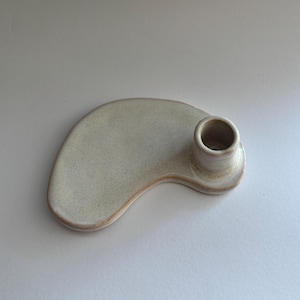Op de afbeelding: Een witte keramische kaarsenhouder met een unieke, organische vorm. De houder heeft een enkele, ronde opening voor een kaars.