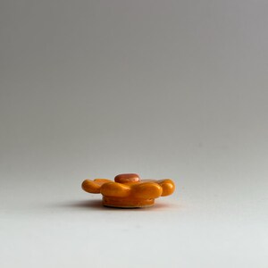 May include: A small, orange ceramic flower with a raised centre. The flower has six petals and is about 5 cm in diameter.