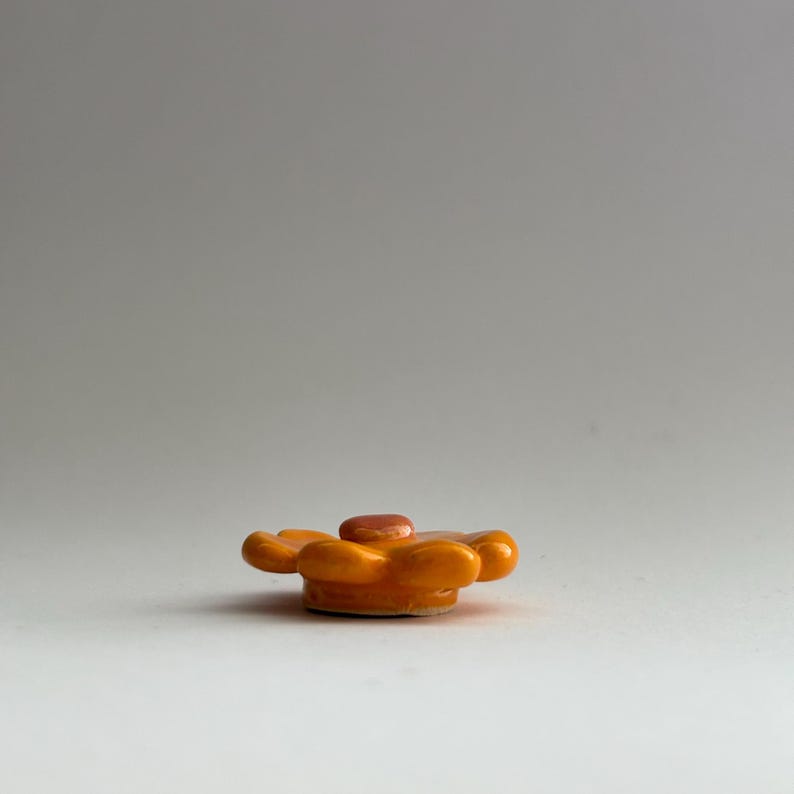 May include: A small, orange ceramic flower with a raised centre. The flower has six petals and is about 5 cm in diameter.