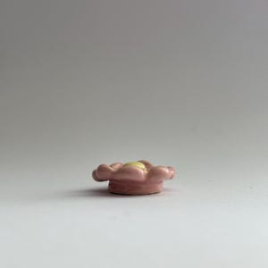 May include: A small pink ceramic flower with a yellow centre. The flower is a decorative object.